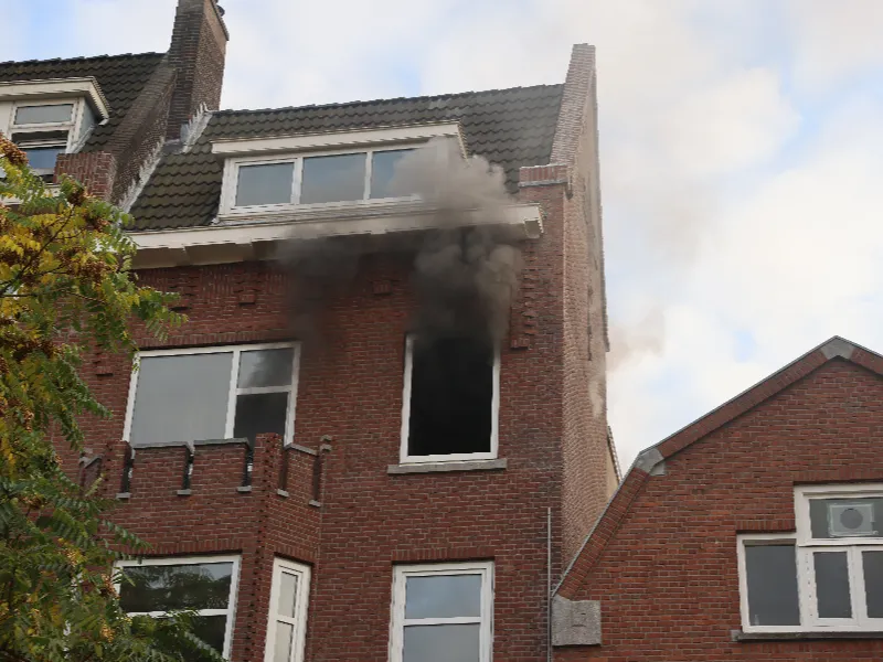 Black smoke billows from a second-floor window of a brick building.