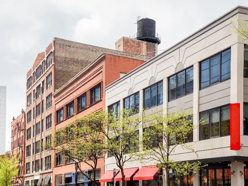 Row of multi-story brick and concrete buildings with trees and red awnings in front.